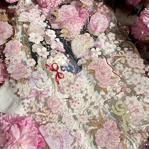 Puede incluir: Una bandeja decorativa con un dise&ntilde;o floral que presenta flores de cerezo rosas y detalles dorados. La bandeja est&aacute; hecha de vidrio transparente y tiene una est&eacute;tica delicada y femenina.