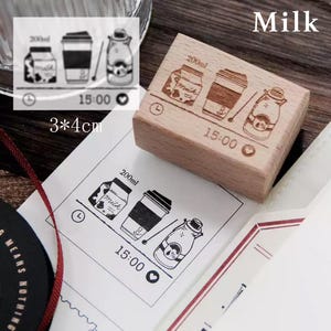 May include: A wooden stamp with a design of a milk carton, a cup of coffee, and a milk bottle. The stamp is 3 by 4 centimeters and has the text "200ml", "Milk", "15:00", and a heart symbol.