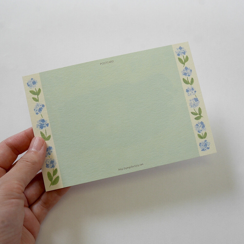 May include: A light green postcard with a floral border of blue flowers and green leaves. The text "POSTCARD" is printed in the top center of the card. The text "http://nakyfactory.net" is printed in the bottom center of the card.