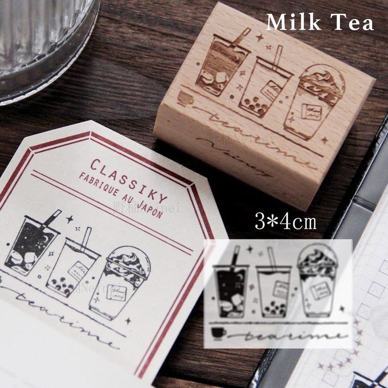 May include: Wooden stamp with a design of three cups of milk tea with boba. The stamp is 3 inches by 4 inches and says "Milk Tea" and "teatime" in cursive. The stamp is made in Japan and is part of the "CLASSIKY" brand.
