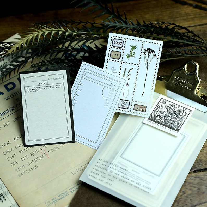 May include: A set of vintage-style paper stickers with illustrations of plants, a frog, and a compass. The stickers are printed on white paper with black ink and have a distressed look. The stickers are perfect for adding a touch of whimsy to journals, planners, and other paper crafts.