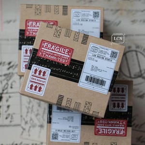 May include: Several small, brown cardboard boxes with shipping labels and red "Fragile" and "This Side Up" stickers. The boxes have black tape and decorative patterns. The text "LCN Design Studio" is visible on the labels.