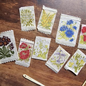 Peut inclure: Une collection de patchs floraux brodés de différentes couleurs, dont le rouge, le bleu, le jaune et le violet, sur un tissu clair. Les patchs présentent des motifs détaillés de fleurs et de feuillage, avec un bord festonné. Les patchs sont disposés sur une surface en bois.