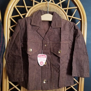 May include: A brown corduroy jacket with a button fastening and two flap pockets. The jacket has a label that reads "TISSU GRAND TINT 100% COTON LAVABLE TAB".