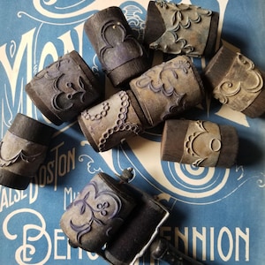 May include: A collection of vintage wooden printing blocks with intricate designs, including floral patterns, swirls, and geometric shapes. The blocks are arranged on a blue surface with a vintage printing roller.