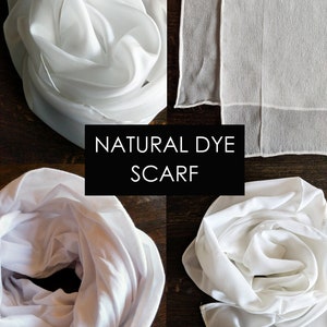 May include: Four white silk scarves, two folded and two laid flat, on a wooden surface. The scarves are natural dye and have a soft, flowing texture. The text "NATURAL DYE SCARF" is displayed in the center of the image.