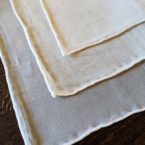 May include: Three white sheer fabric squares with a white trim around the edges. The squares are stacked on top of each other.