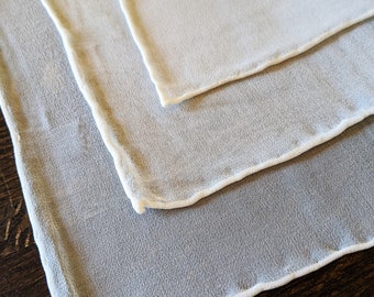 May include: Three white sheer fabric squares with a white trim around the edges. The squares are stacked on top of each other.