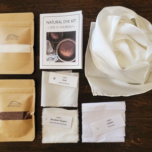 May include: Natural dye kit with instructions, two brown paper bags containing dye, and three white fabric swatches labeled "Silk", "Bamboo Rayon", and "Cotton".