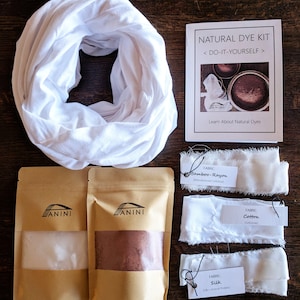 May include: Natural dye kit with three fabric swatches, two brown paper bags with white and brown powder, and a white scarf. The fabric swatches are labeled "Bamboo-Rayon", "Cotton", and "Silk". The bags are labeled "ANINI". The instruction booklet says "NATURAL DYE KIT < DO-IT-YOURSELF > Learn About Natural Dyes".
