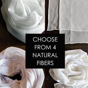 Op de afbeelding: Vier witte vierkante stoffen, elk gevouwen en op een andere manier gerangschikt. De vierkante stoffen zijn gemaakt van natuurlijke vezels. De tekst "CHOOSE FROM 4 NATURAL FIBERS" wordt in het midden van de afbeelding weergegeven.