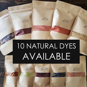 Op de afbeelding: Tien bruine papieren zakjes met het woord "ANNINI" erop gedrukt. Elk zakje bevat een ander natuurlijk kleurpoeder. De zakjes zijn gerangschikt in twee rijen van vijf. De tekst "10 NATURAL DYES AVAILABLE" is in wit op een zwarte achtergrond gedrukt.