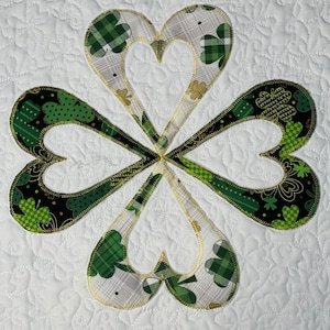 May include: A four-leaf clover quilt block with green and gold fabric. The clover is made of four hearts with a white background.