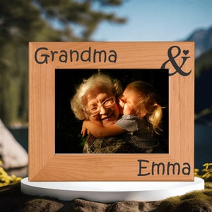 May include: A wooden picture frame with the words "Grandma & Emma" engraved on it. A photo of a grandmother and granddaughter hugging is inside the frame.