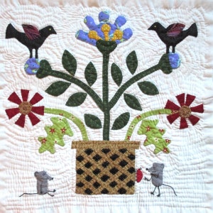 May include: A quilted wall hanging featuring a stylized plant with blue, yellow, and green flowers, two black birds perched on the branches, and two gray mice at the bottom. The plant is in a brown and black checkered pot.