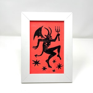 Op de afbeelding: Een zwart silhouet van een duivel met hoorns en een drietand op een felrode achtergrond met zwarte sterren.