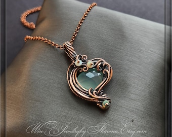 May include: A copper-colored wire-wrapped pendant necklace with a heart-shaped, pale green gemstone. The pendant is adorned with small, round, white beads and intricate wire detailing. The necklace chain is also copper-colored.