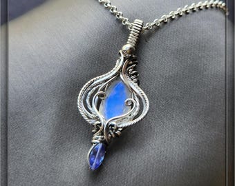 May include: A silver pendant necklace with a teardrop-shaped, iridescent blue gemstone. The pendant is intricately wire-wrapped with a delicate design, and the necklace has a silver chain. The text "Wire Jewelry by Shawna. Etsy.com" is at the bottom.