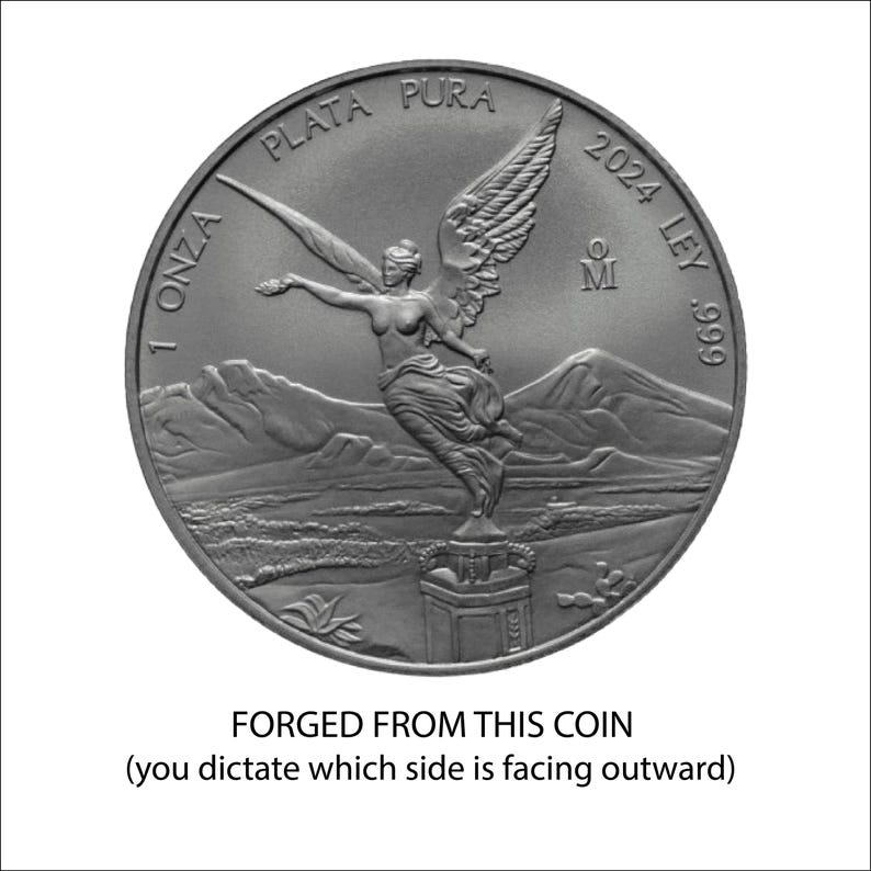 The image is a silver coin with an embossed figure of a winged woman, standing on a pedestal with mountains in the background. The coin is described as "FORGED FROM THIS COIN" and "you dictate which side is facing outward".