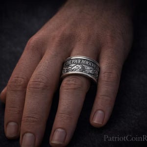 A close-up of a person's hand wearing a silver ring with engraved text.