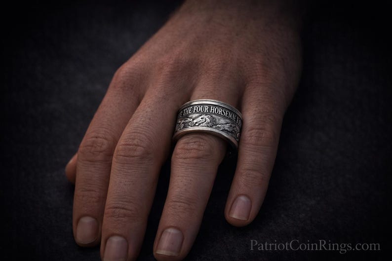 A close-up of a person's hand wearing a silver ring with engraved text.