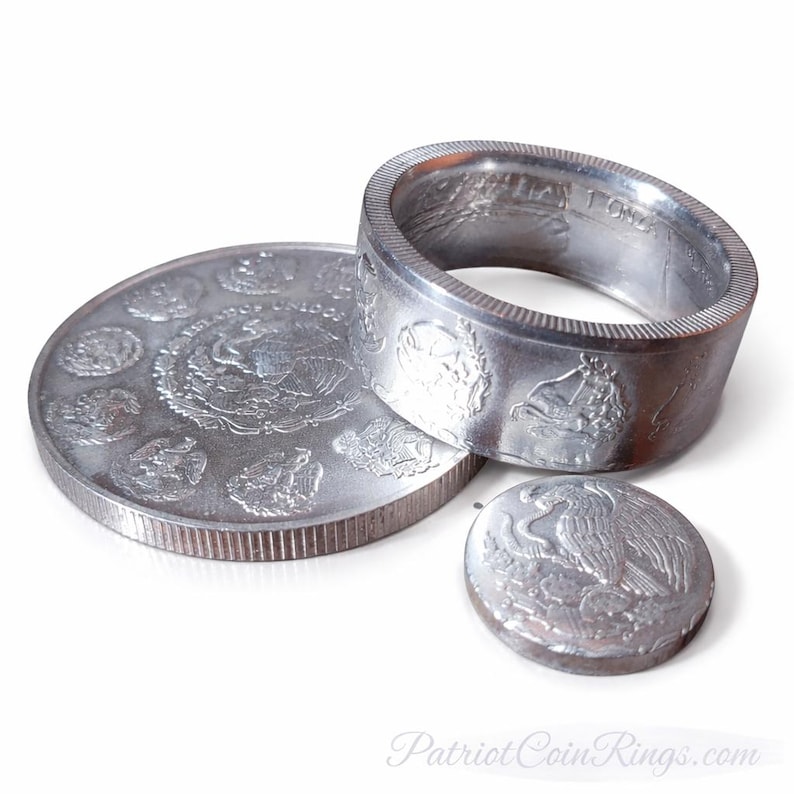 a collection of silver coins and a ring, including a large silver coin with an embossed design and a smaller silver coin with an embossed design.
