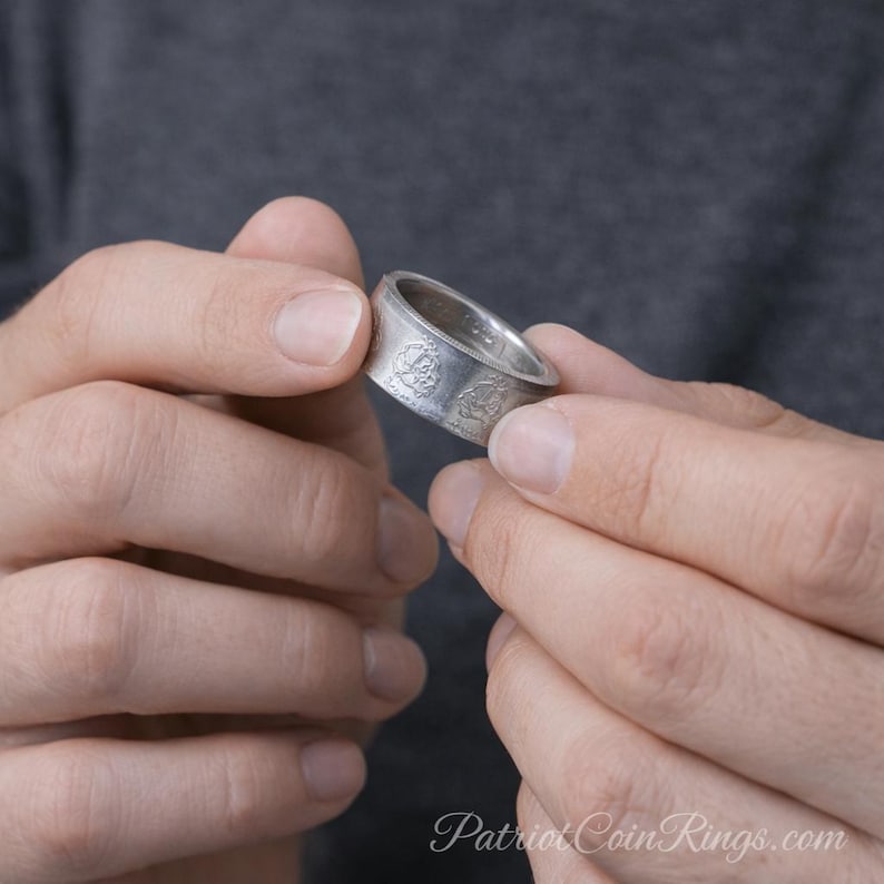 A person's hands holding a silver ring with a design on it.
