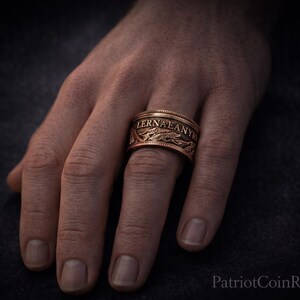 A close-up of a person's hand wearing a ring with the word "LERNA" engraved on it.