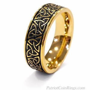 Könnte beinhalten: Goldfarbener Ring mit einem schwarzen keltischen Knotenmuster. Der Ring hat eine polierte Oberfläche und ein Band mit einem komplizierten Muster. Die Website PatriotCoinRings.com ist sichtbar.