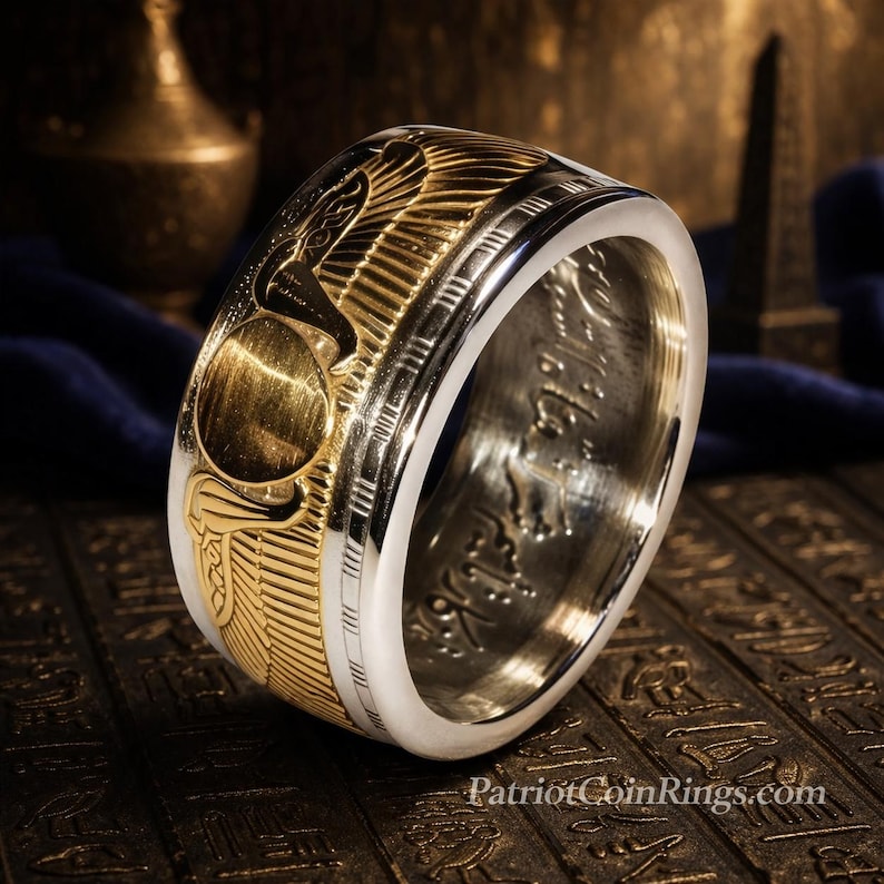 A silver ring with intricate designs and patterns, including a snake motif, is displayed on a dark surface with a blurred background.