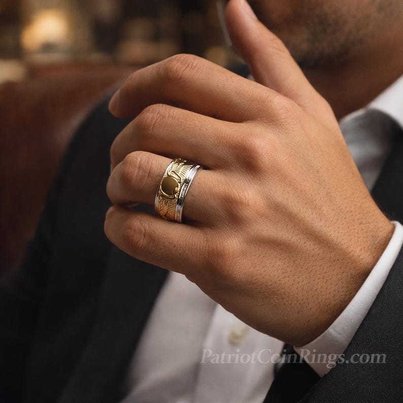 A close-up of a person's hand wearing a gold ring on the ring finger, with a blurred background.