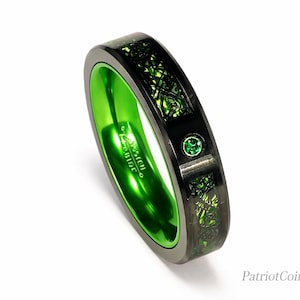 May include: A black tungsten carbide ring featuring a vibrant green inner band and a central inlay with a green textured pattern. The exterior surface includes a small circular green gemstone accent. The text Tungsten Carbide is engraved inside.