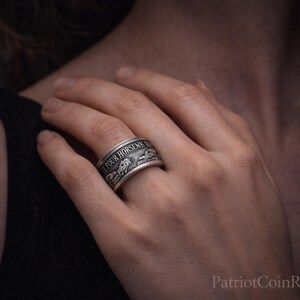 A close-up of a person's hand wearing a silver ring with a decorative design.