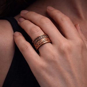 A close-up image of a person's hand wearing a gold-colored ring with a decorative design.