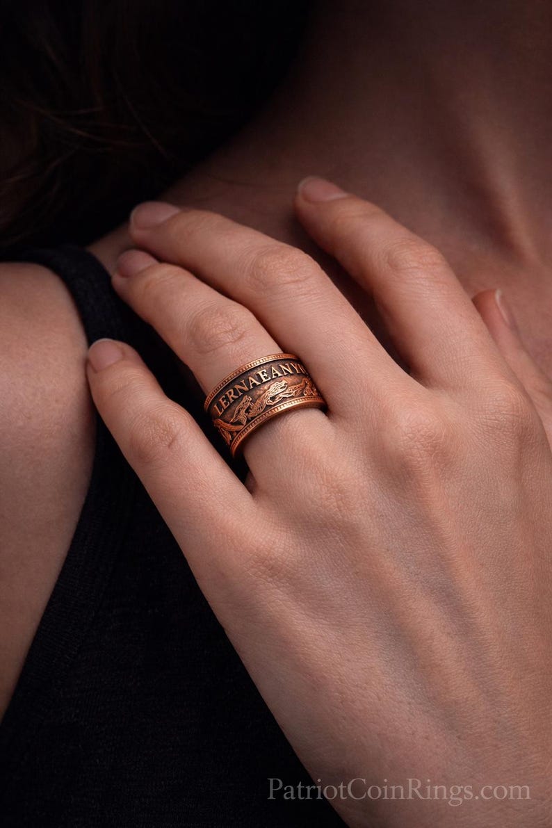 A close-up image of a person's hand wearing a gold-colored ring with a decorative design.