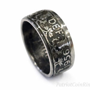 May include: A silver-toned ring with engraved details, including the year 1956 and the letters DEF. The ring features floral and star-like designs. The ring is displayed against a white background.