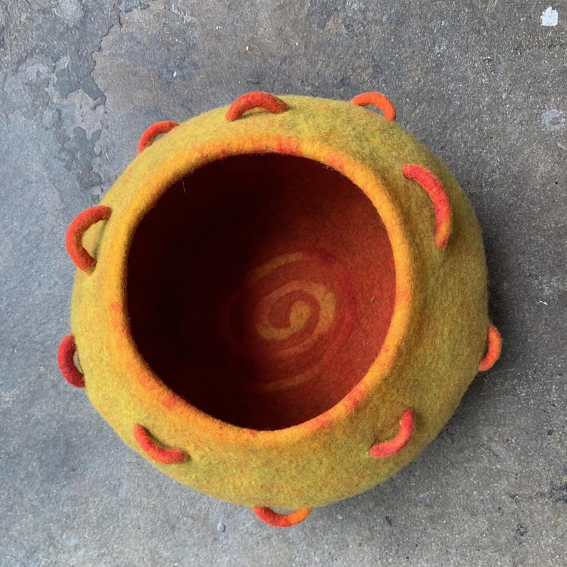 Felted vessel, pure wool. Orange on the inside with a spiral on the bottom. Green on the outside with at multitude of orange handles, a climbing wall.