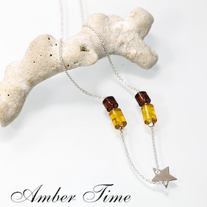 May include: A silver chain necklace with two amber beads and a silver star charm. The necklace is displayed on a piece of white coral. The text "Amber Time" is written below the necklace.