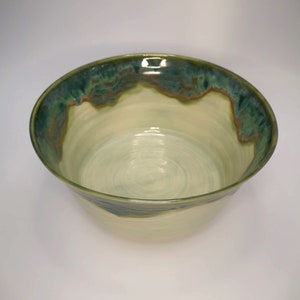 Op de afbeelding: Een grote, keramische kom met een lichtgroene glazuur en een donkergroene rand. De kom heeft een subtiel swirl-patroon aan de binnenkant.