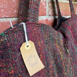 K&ouml;nnte beinhalten: Eine schwarze, mehrfarbige gewebte Tragetasche mit einem braunen Etikett, auf dem "Made in Nepal" steht.
