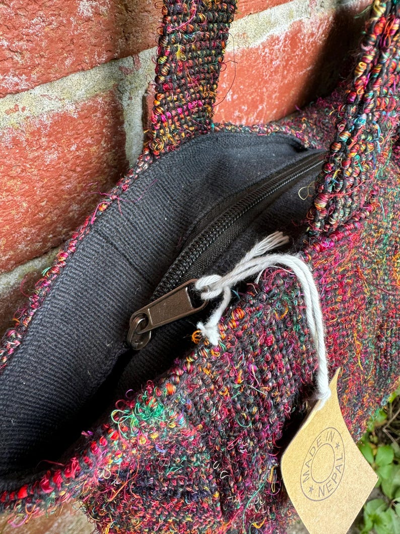 K&ouml;nnte beinhalten: Nahaufnahme einer bunten gewebten Tragetasche mit einer schwarzen Rei&szlig;verschlusstasche und einem braunen Etikett mit der Aufschrift "Made in Nepal".