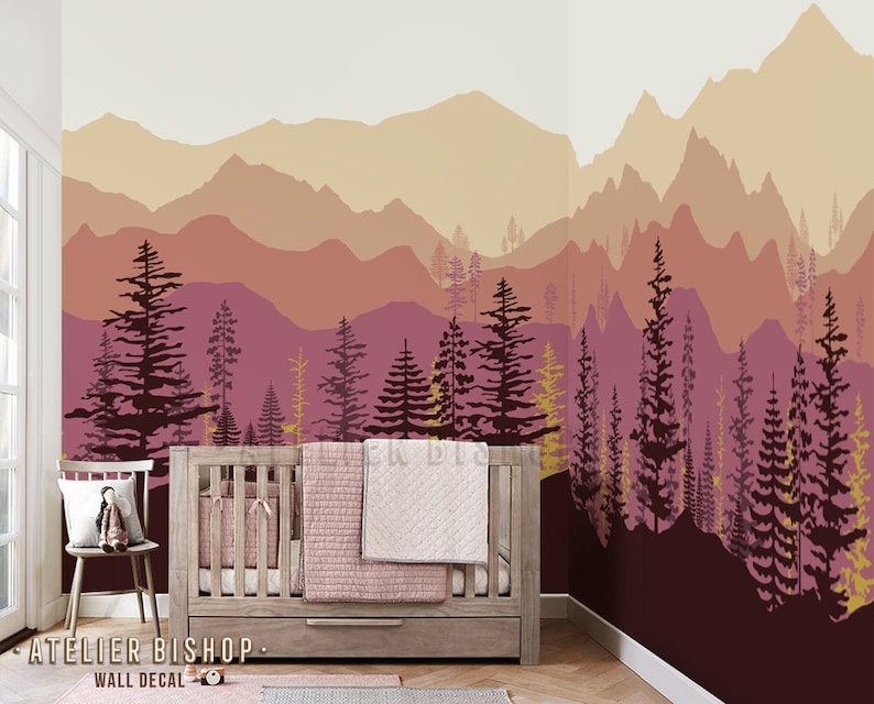 May include: A nursery wall decal featuring a silhouette of a mountain range with a forest in the foreground. The mountains are in shades of pink, orange, and yellow, while the trees are dark brown and yellow. The decal is perfect for adding a touch of nature to a child's room.