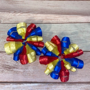 May include: Two red, blue, and yellow ribbon bows with a mesh center. The bows are tied together in the center.