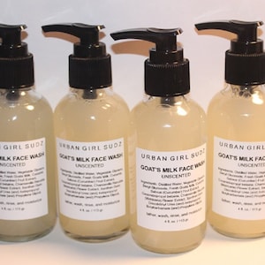 Peut inclure: Quatre flacons en verre transparent avec des pompes noires remplis d'un liquide jaune clair. Chaque flacon porte une étiquette blanche avec le texte "URBAN GIRL SUDZ GOAT'S MILK FACE WASH UNSCENTED" et une liste d'ingrédients.