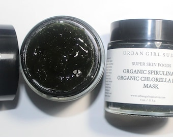 Può includere: Un barattolo di maschera per il viso verde scuro con il coperchio aperto, accanto al coperchio. Il barattolo ha un'etichetta che recita "URBAN GIRL SUDZ ORGANIC SPIRULINA & ORGANIC CHLORELLA FACE MASK". Il barattolo contiene 113 g di prodotto.