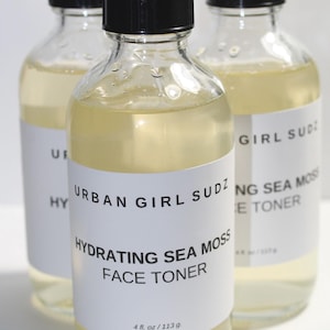 Könnte beinhalten: Drei durchsichtige Glasflaschen mit schwarzen Deckeln und weißen Etiketten. Die mittlere Flasche trägt die Aufschrift "URBAN GIRL SUDZ HYDRATING SEA MOSS FACE TONER 4 fl. oz/113g".