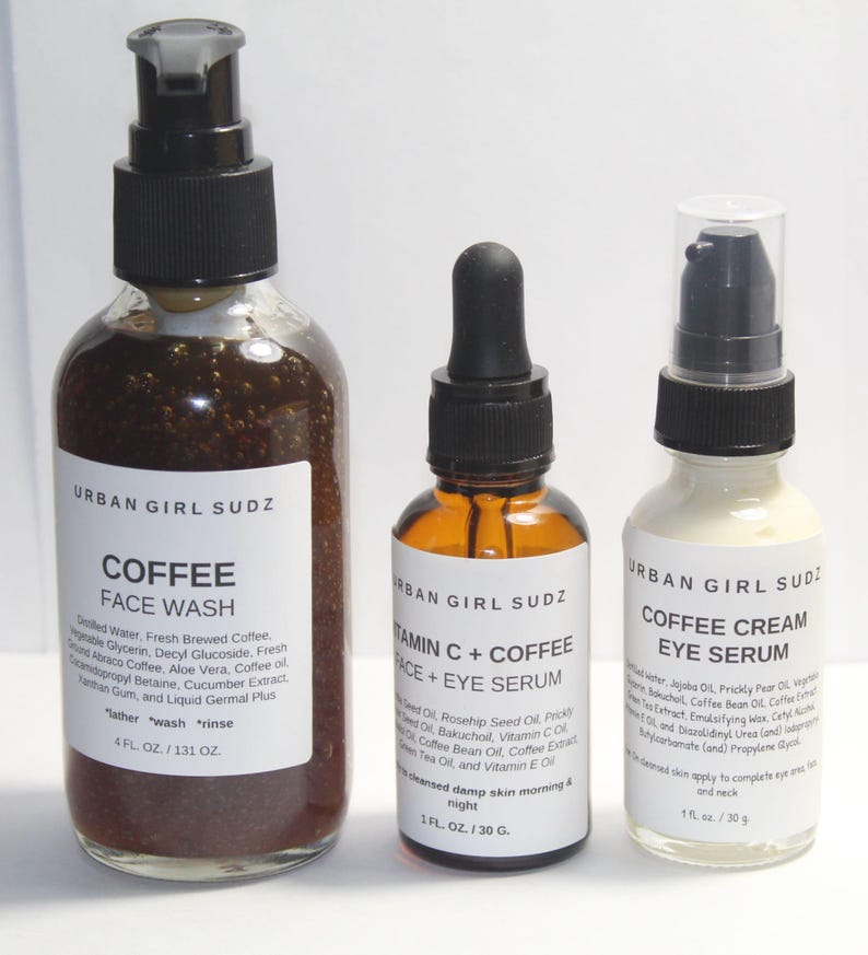 May include: Three glass bottles with black pump tops and labels. The bottles contain coffee face wash, vitamin C and coffee face and eye serum, and coffee cream eye serum. The labels are white with black text and the brand name "Urban Girl Sudz".