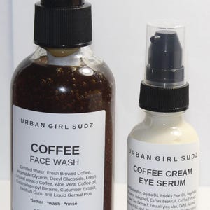 May include: Two glass bottles of coffee-based skincare products. The larger bottle is a brown liquid face wash labeled "URBAN GIRL SUDZ COFFEE FACE WASH" with instructions to "lather, wash, rinse". The smaller bottle is a white cream eye serum labeled "URBAN GIRL SUDZ COFFEE CREAM EYE SERUM".