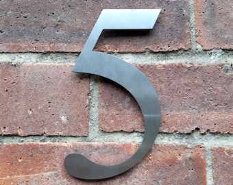 May include: A silver metal house number five is mounted on a brick wall.