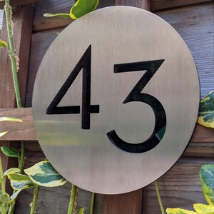 May include: A round, silver metal house number sign with the number 43 in black.